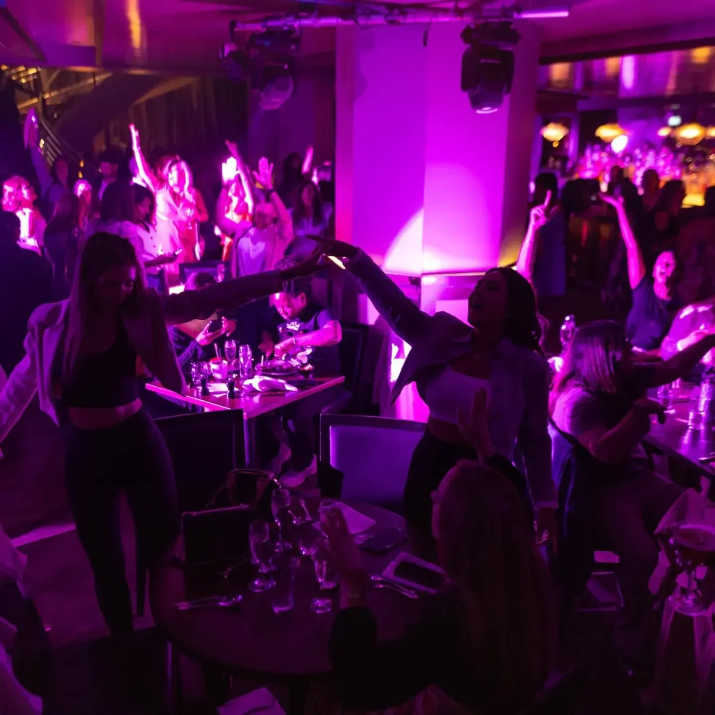Energetic dining and dancing at 100 Wardour St restaurant in London, illuminated with purple lights.