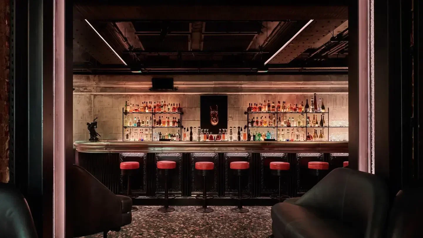 Interior view of the bar at BEAT Club London with red stools and bottles.