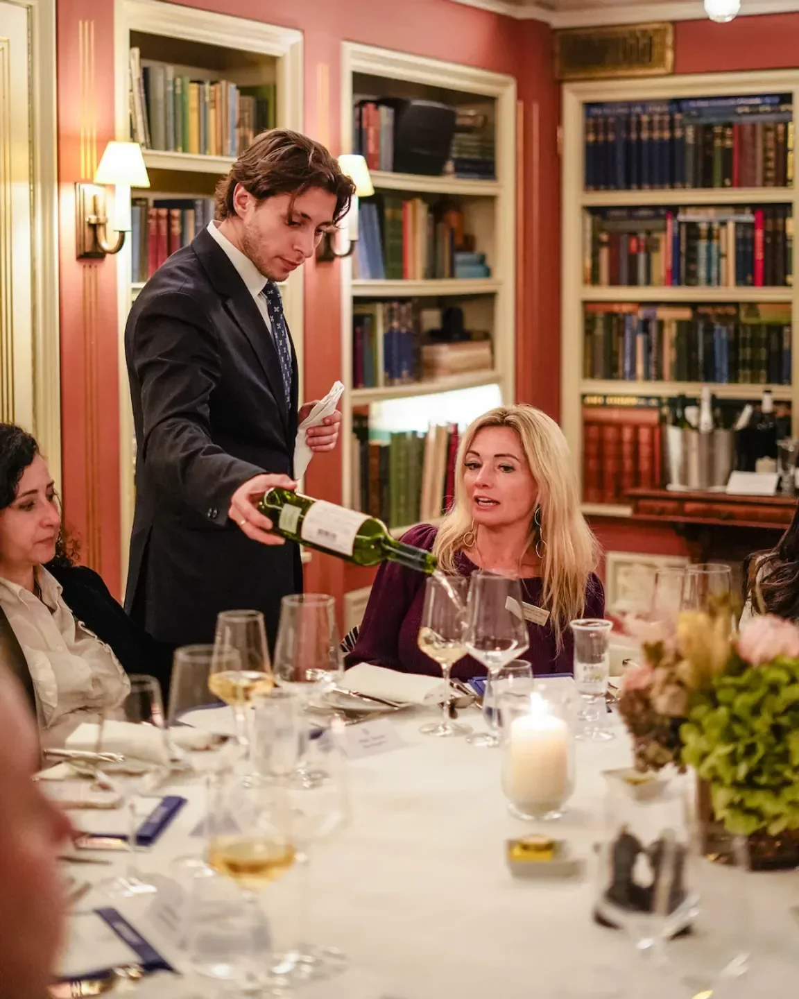 Server pours wine at Bentley's Oyster Bar & Grill in London, with dining guests.