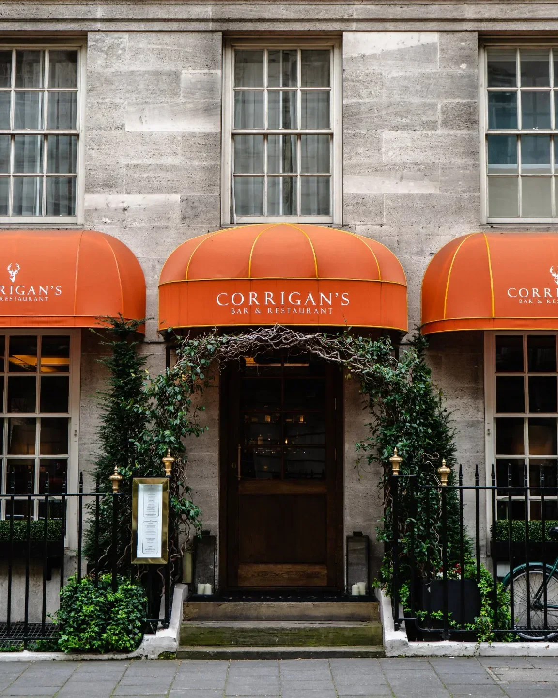 Entrance to Corrigan's Mayfair restaurant in London with orange awnings and greenery.