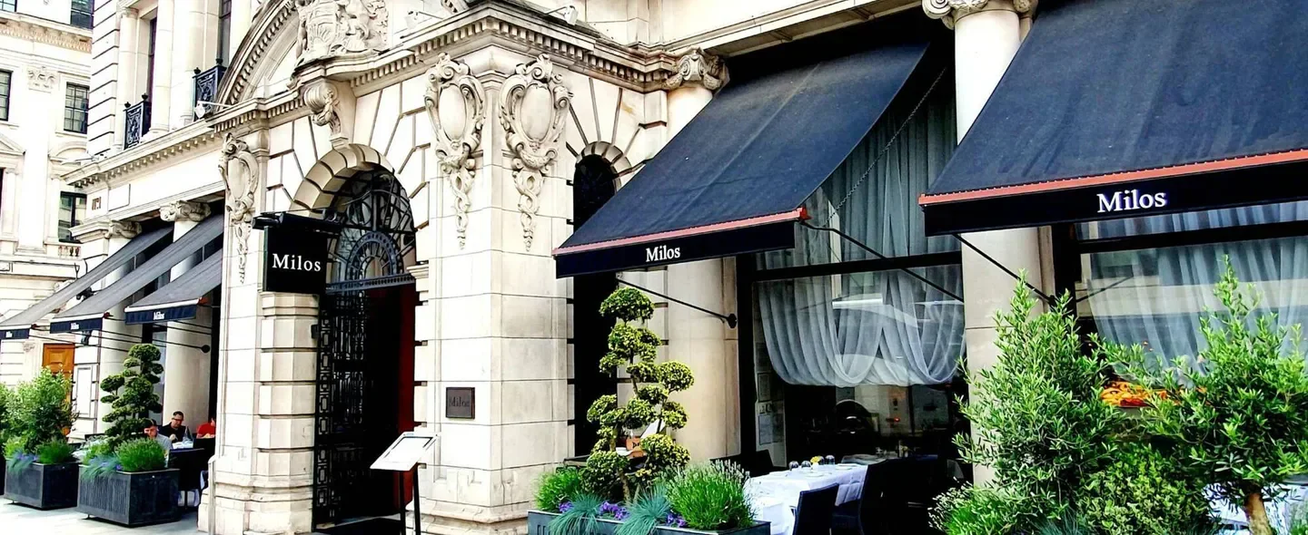 Exterior view of Estiatorio Milos - London restaurant in London, with awnings and greenery.