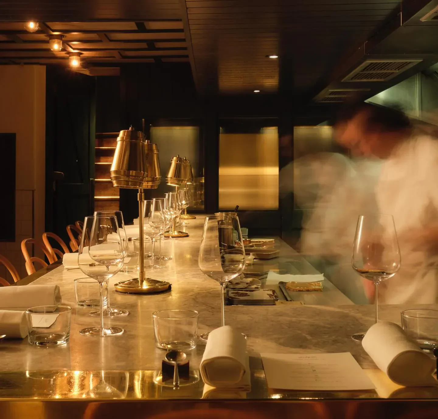 Interior of Evelyn's Table, London, showing bar seating, glasses, and a chef at work.