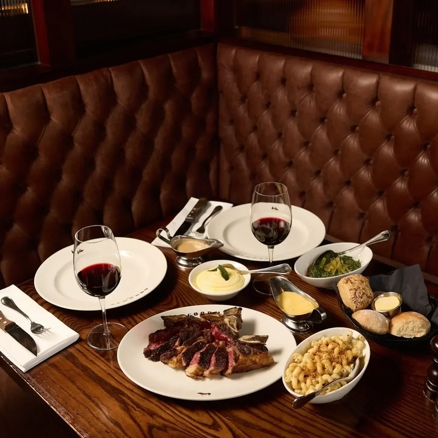 Steak and sides on a table at Goodman London, featuring wine and a cozy booth.