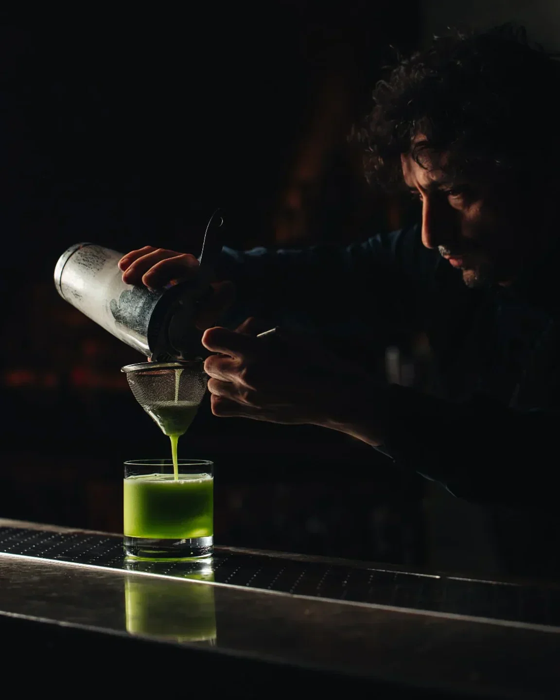 Expert bartender at Hakkasan London pouring a vibrant green cocktail into a glass.