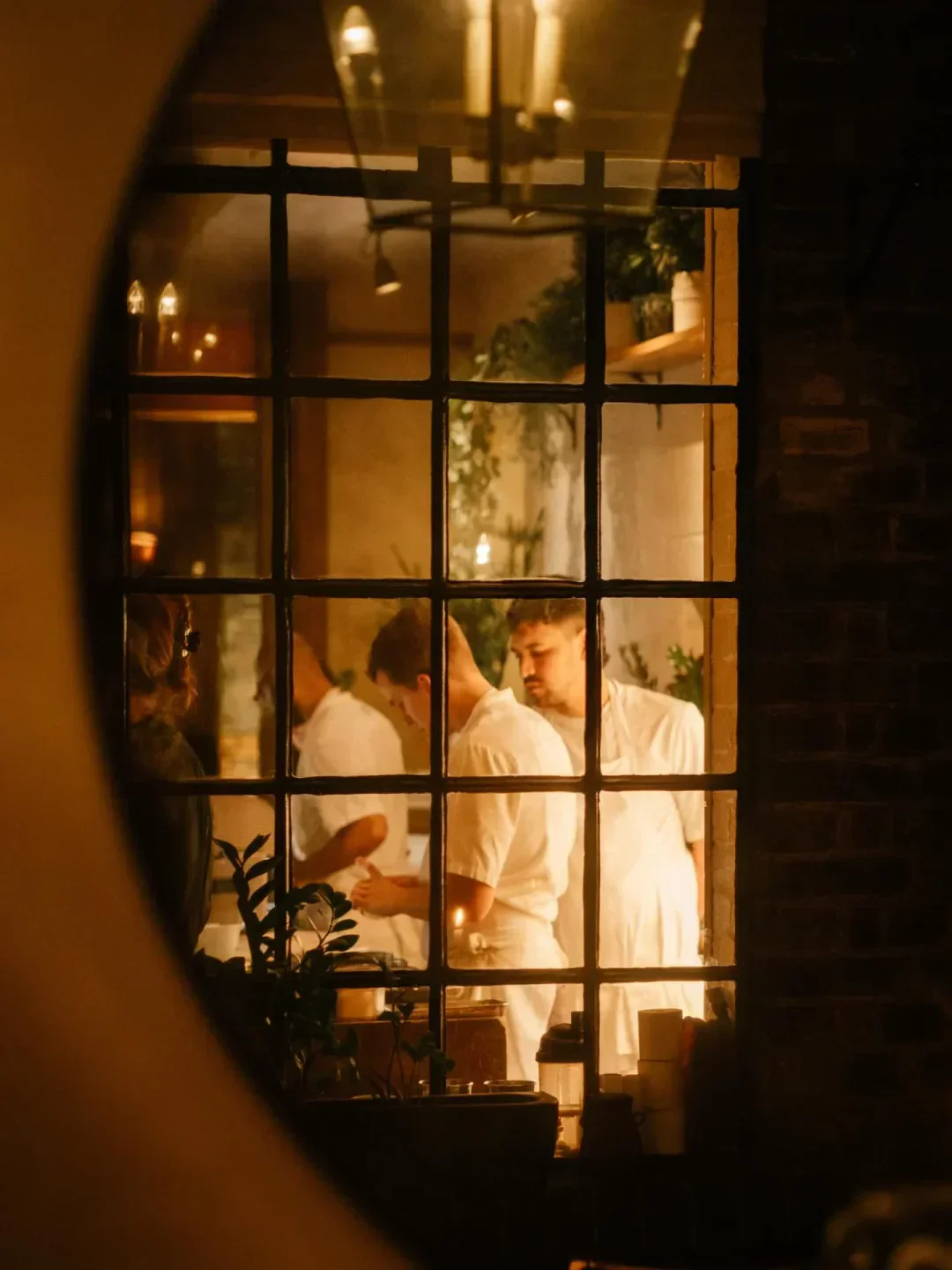 Chefs working in the kitchen at Luca restaurant, framed window view in London.