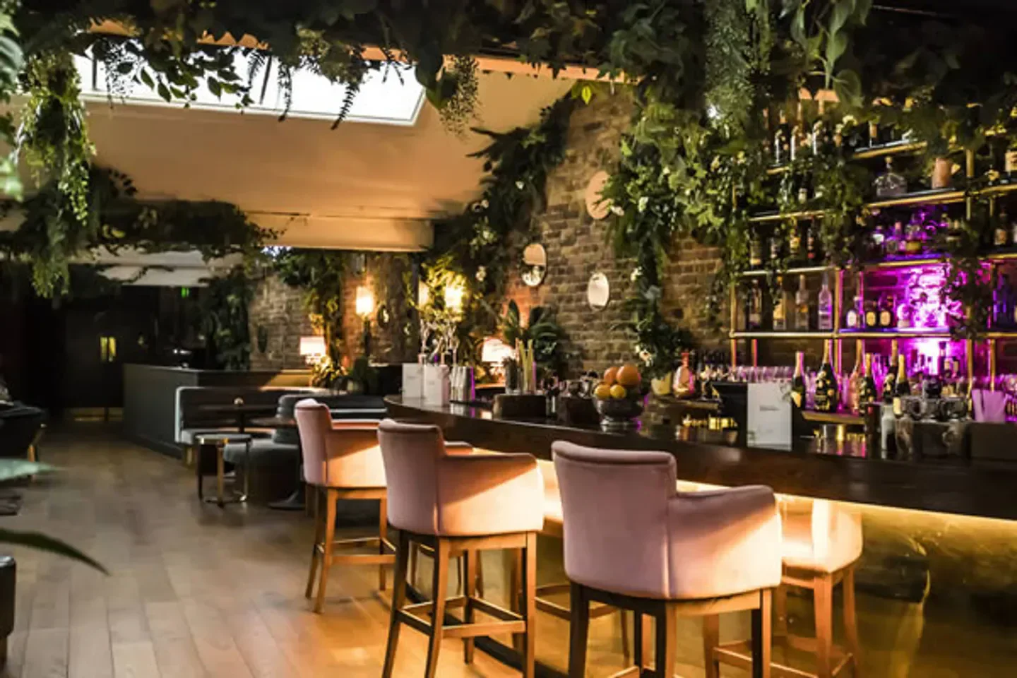 Interior of Ours restaurant in London, with bar stools and a lush, green decor.