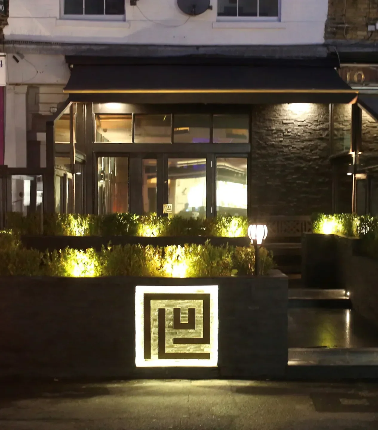 Exterior view of PLU Restaurant in London, illuminated at night with a modern design.