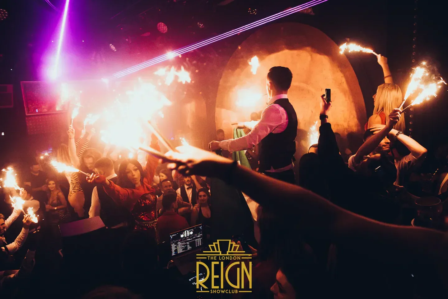 Energetic crowd celebrating at Reign London nightclub with sparklers and DJ