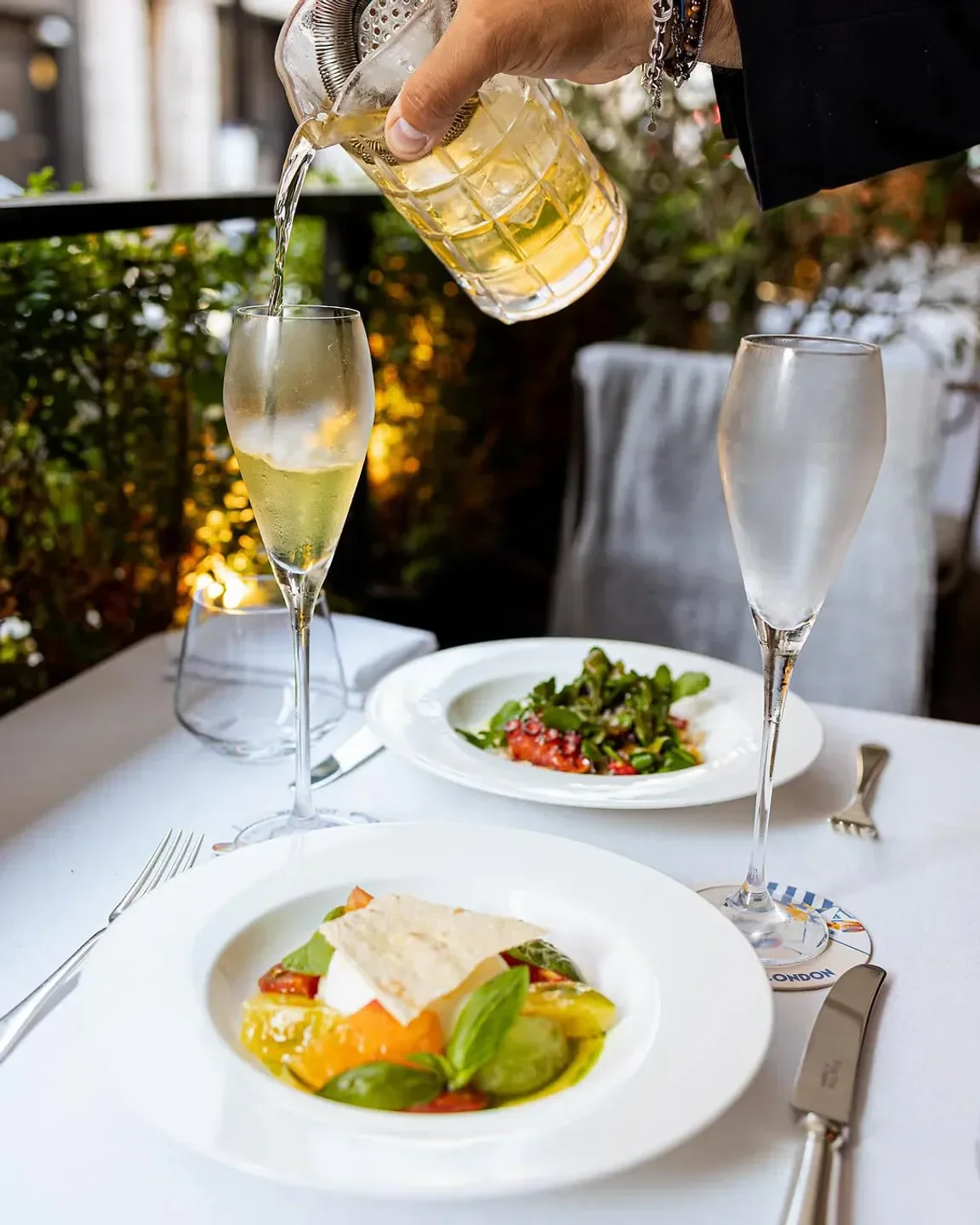 Cocktail being poured into a glass at Sartoria restaurant in London, with food on the table.