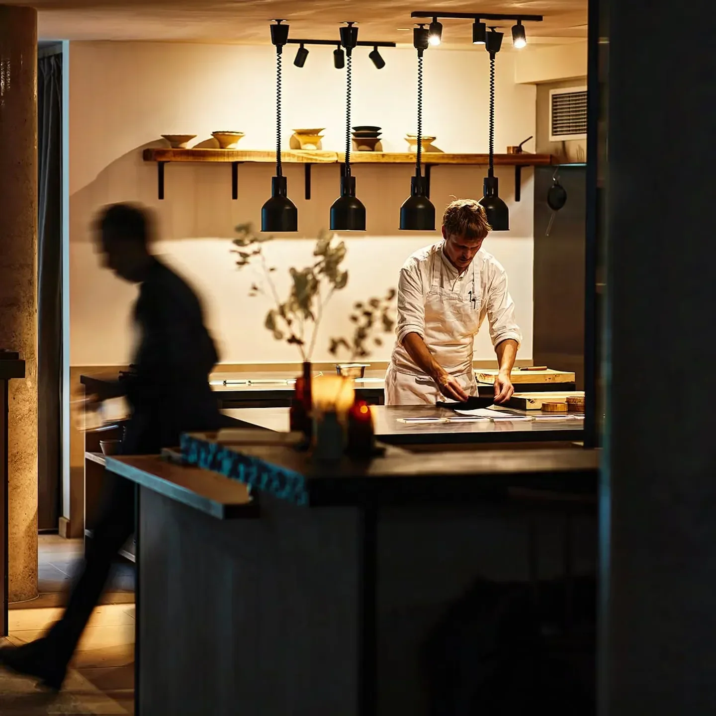 Chef at work in the kitchen of St. Barts restaurant in London, warm lighting.