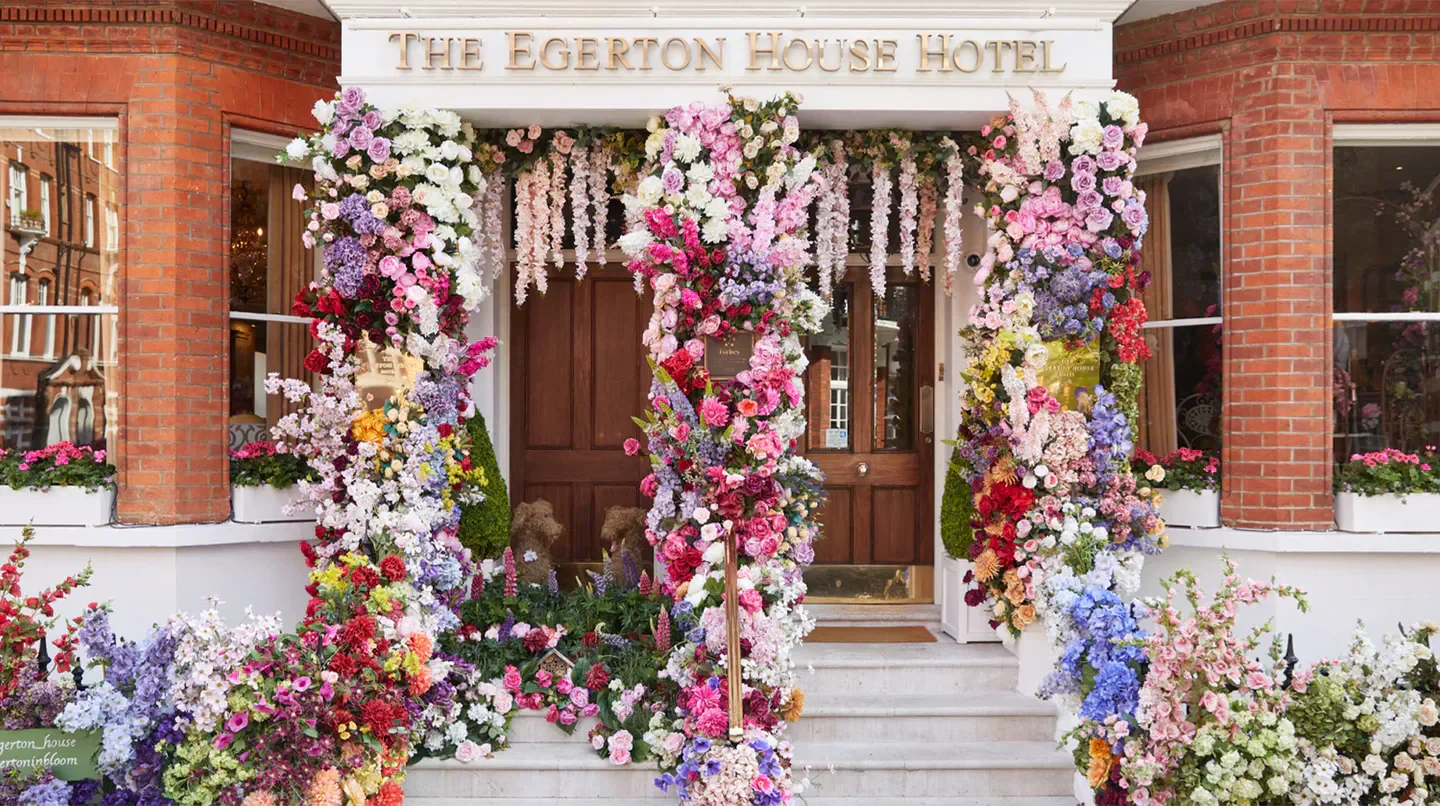 Entrance of The Egerton House Hotel in London, adorned with vibrant floral display