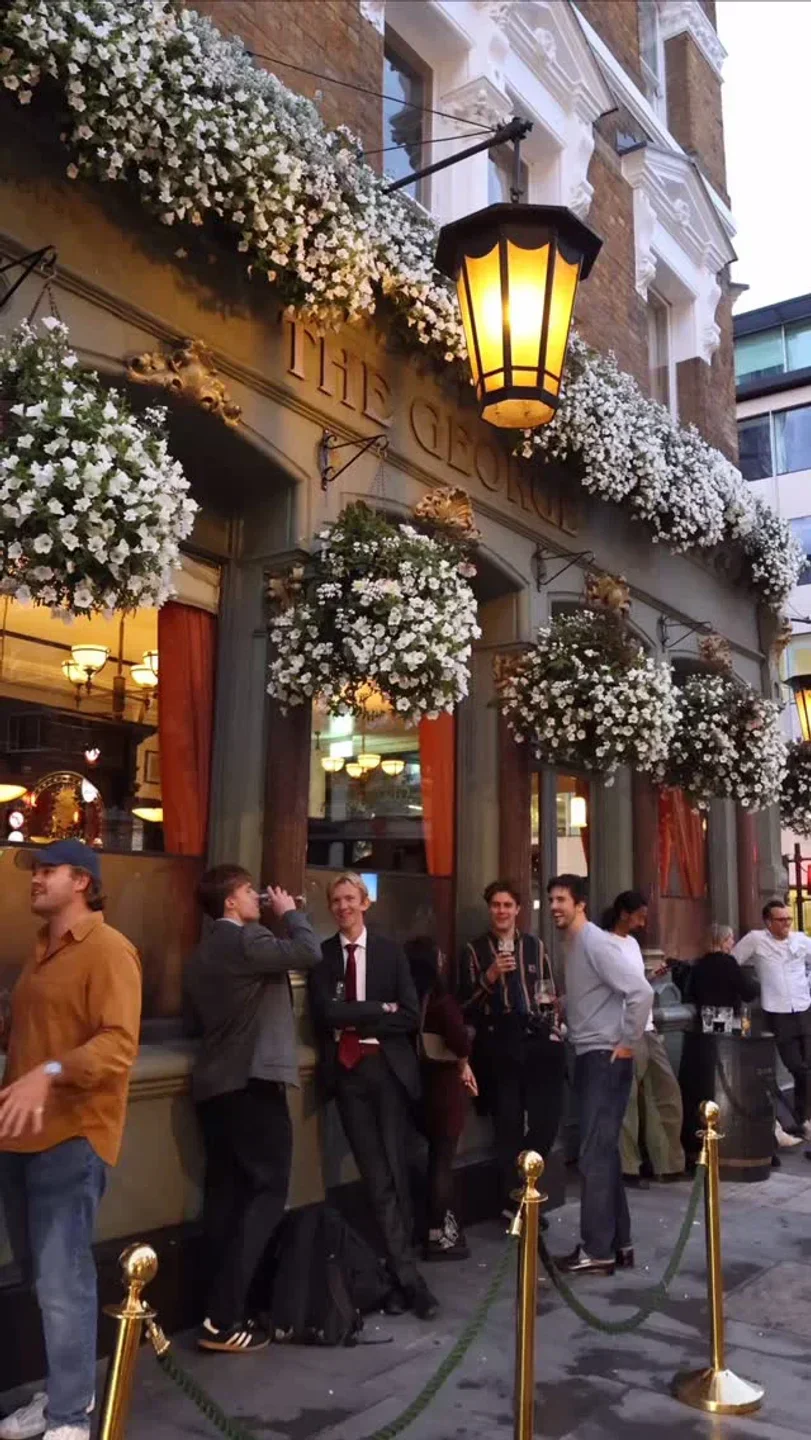 Exterior of The George in London, with floral decor and patrons enjoying drinks.
