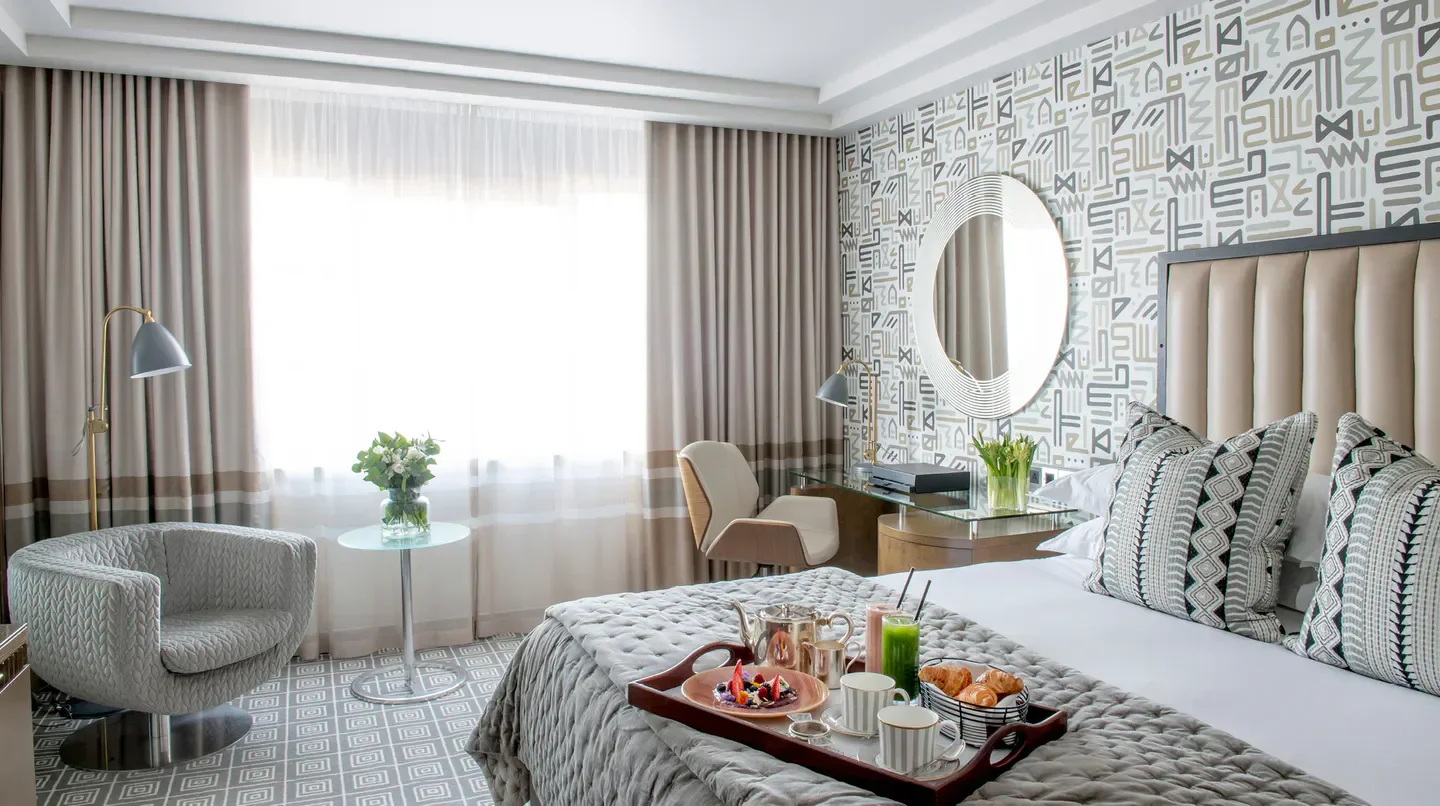 Cozy hotel room at The Marylebone in London, breakfast tray on bed with city views.